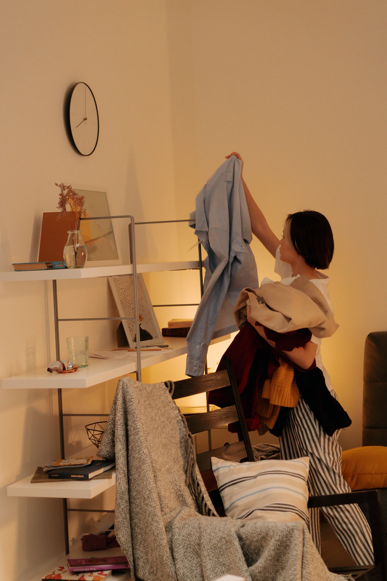 A woman gathering an armful of laundry in a lived-in home