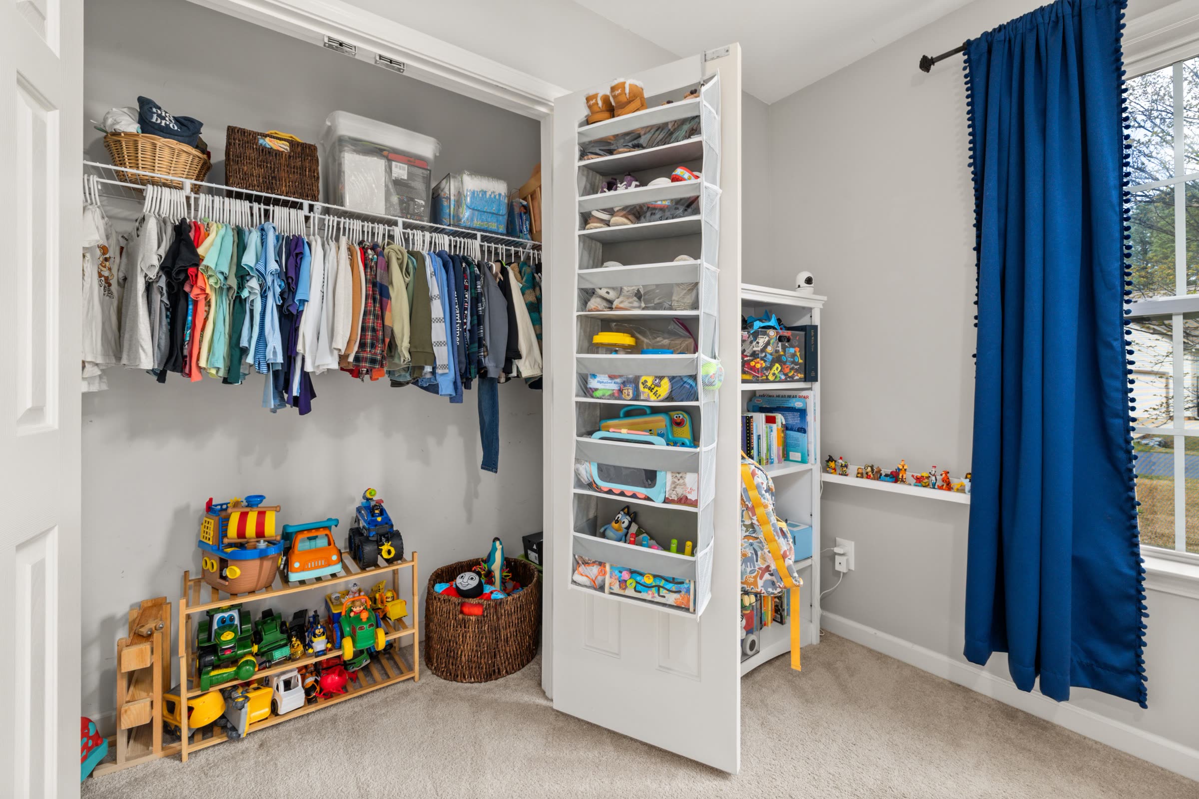 A children's closet with clothing organized by category and a hanging shoe and toy organizer
