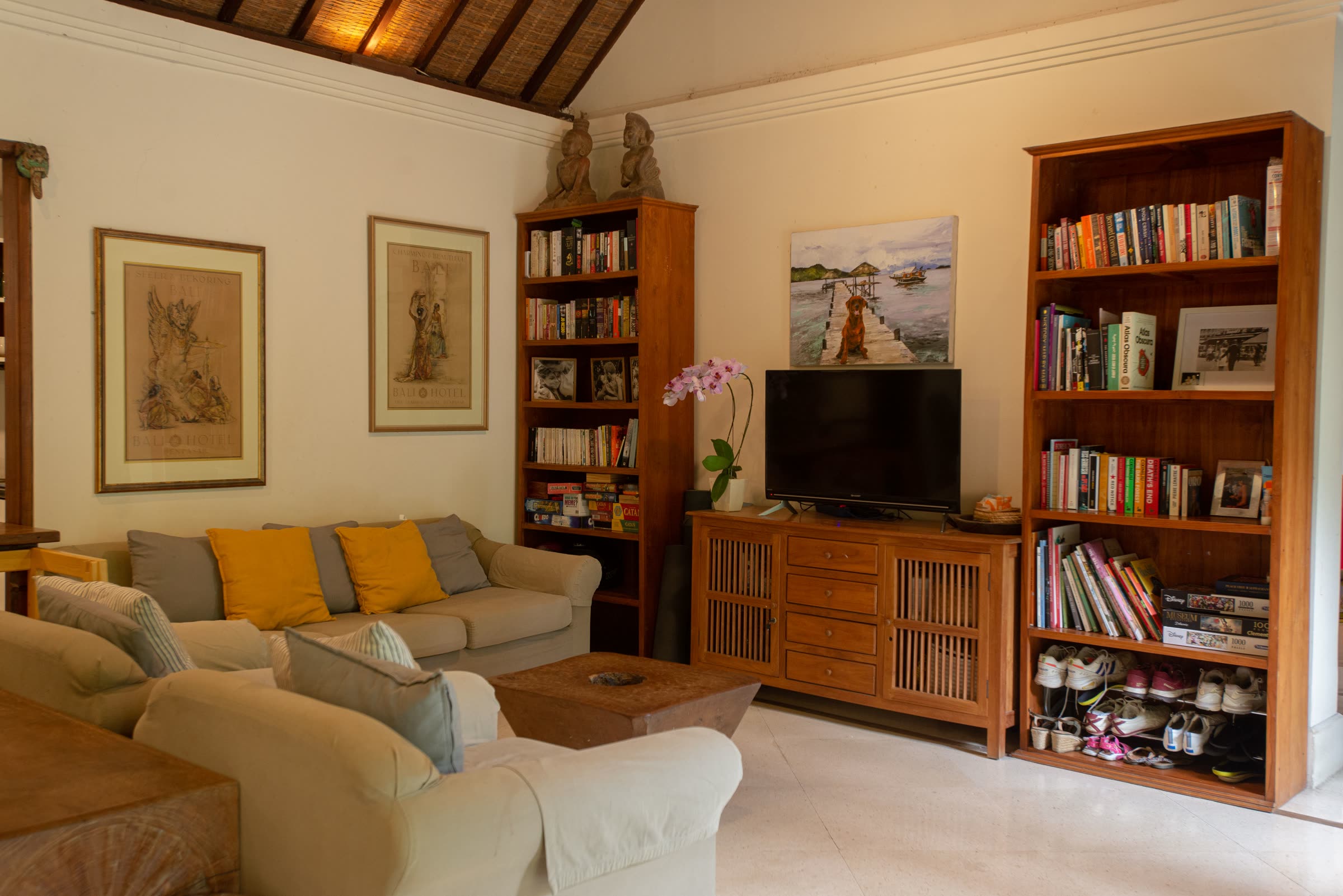 A living room bookshelf with books organized by shelf and a neatly arranged shoe rack below