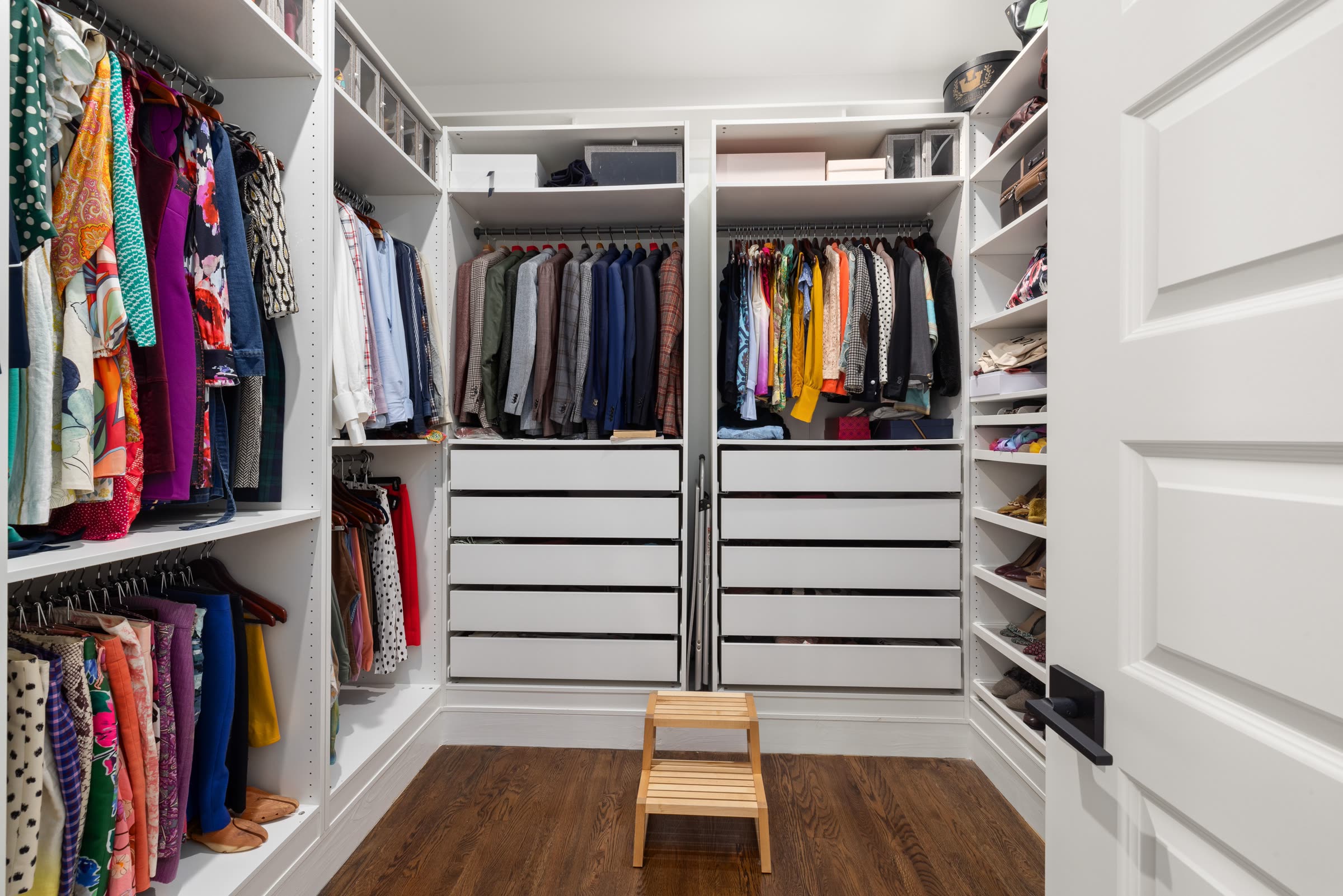 A walk-in closet with clothing sorted by type and color, drawers, and shoe shelving