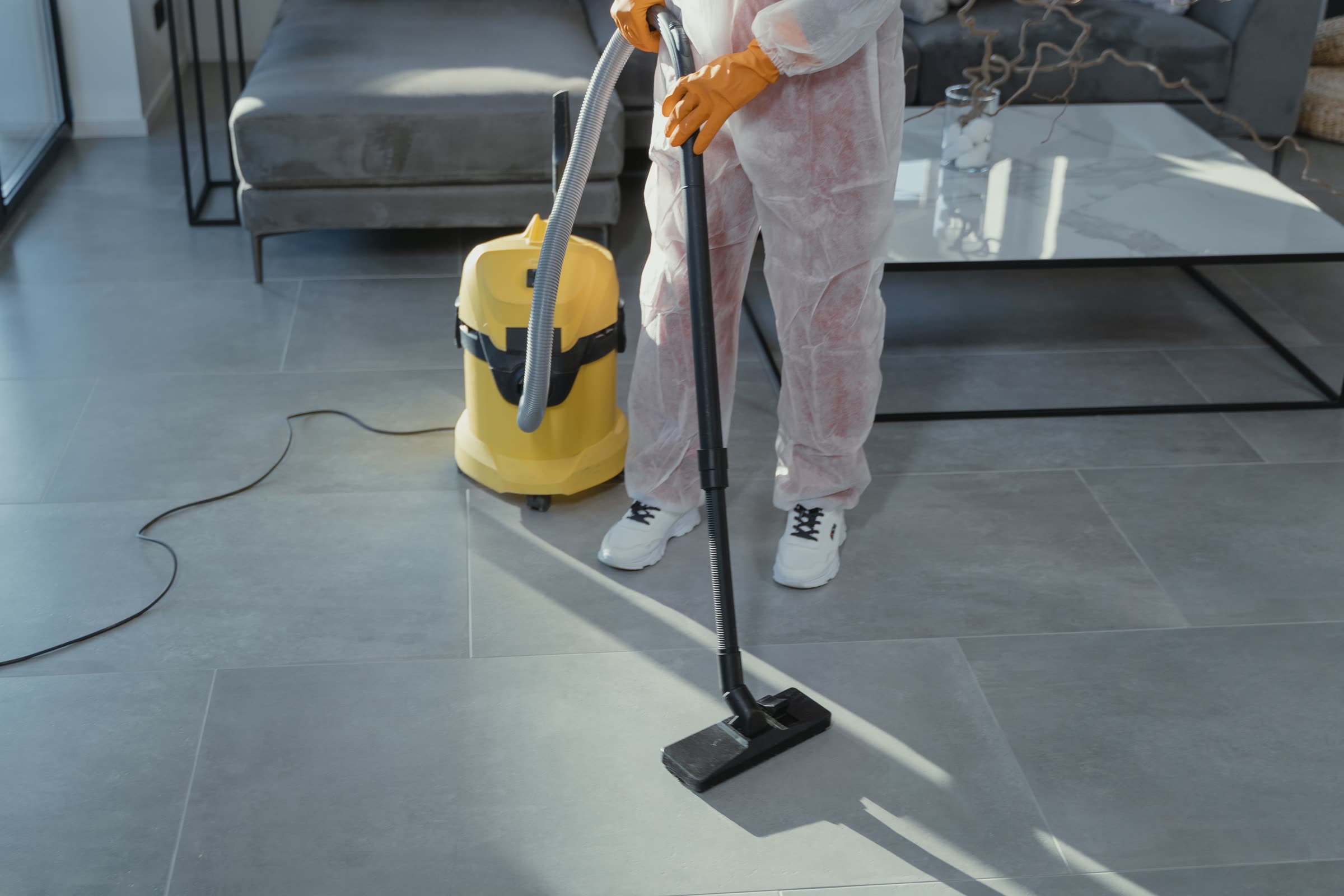 A professional cleaner in protective attire vacuuming a hard floor
